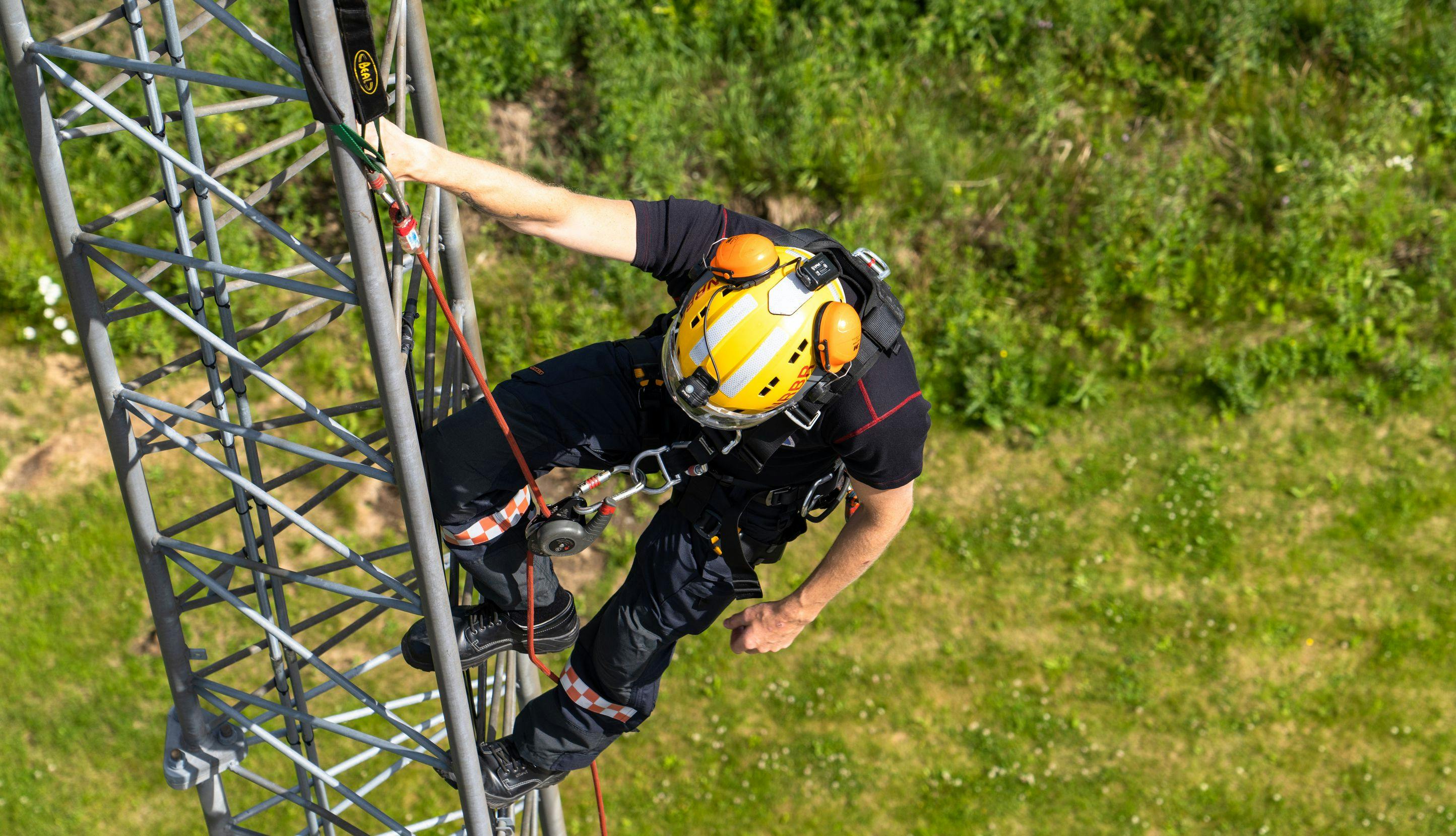Brannkonstabel med hjelm og sikkerhetsutstyr klatrer i mast.
