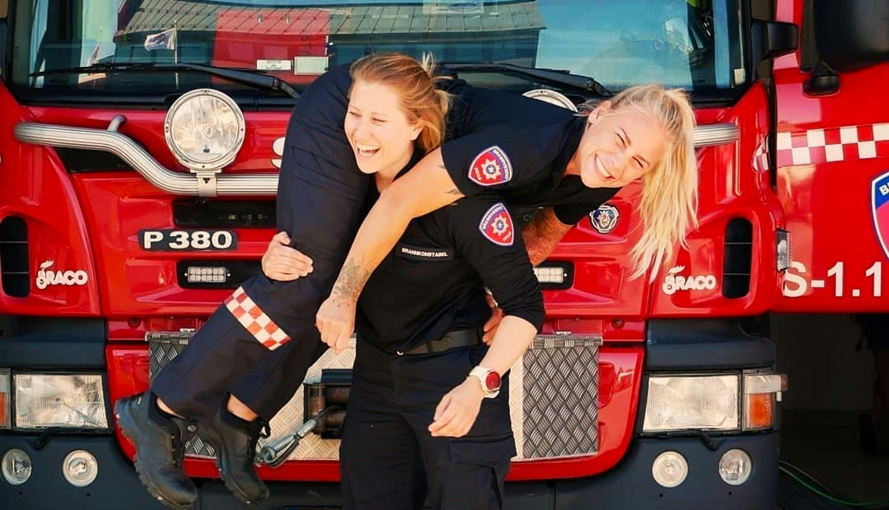 En kvinnelig brannkonstabel løfter en annen kvinnelig brannskonstabel.  
