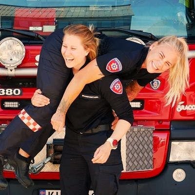 En kvinnelig brannkonstabel løfter en annen kvinnelig brannskonstabel.  