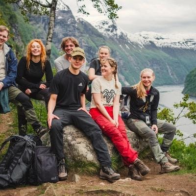 Unge kvinner og menn raster med fjordlandskap i bakgrunnen. 